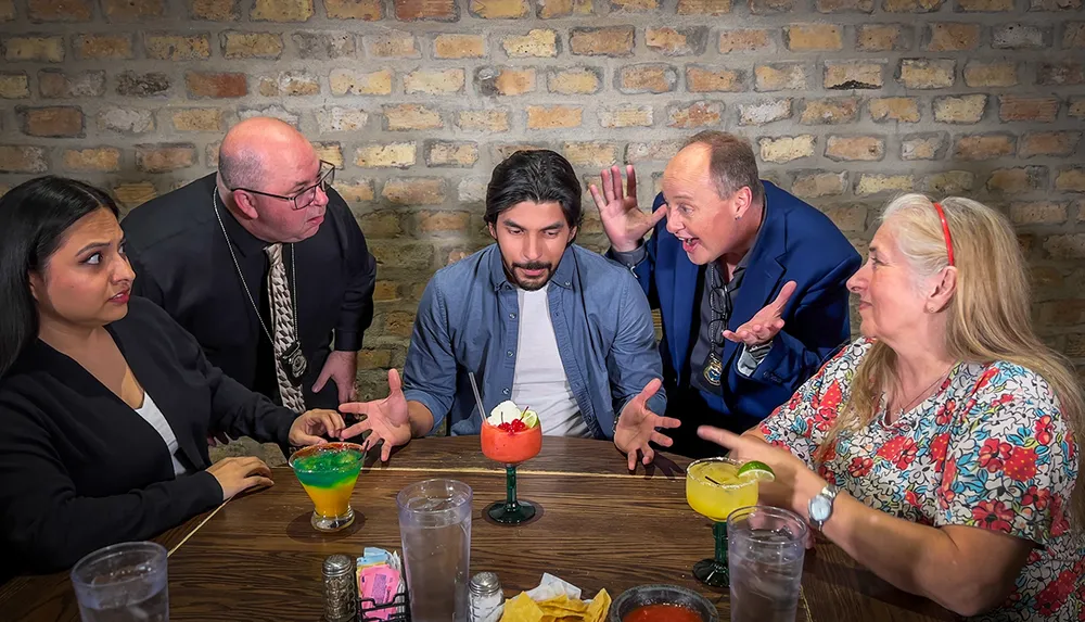 A group of five people are sitting at a table with colorful drinks engaging in an animated discussion