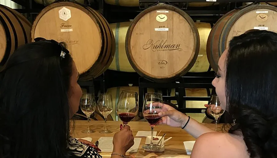 Two individuals are enjoying a wine tasting session in front of wooden wine barrels.