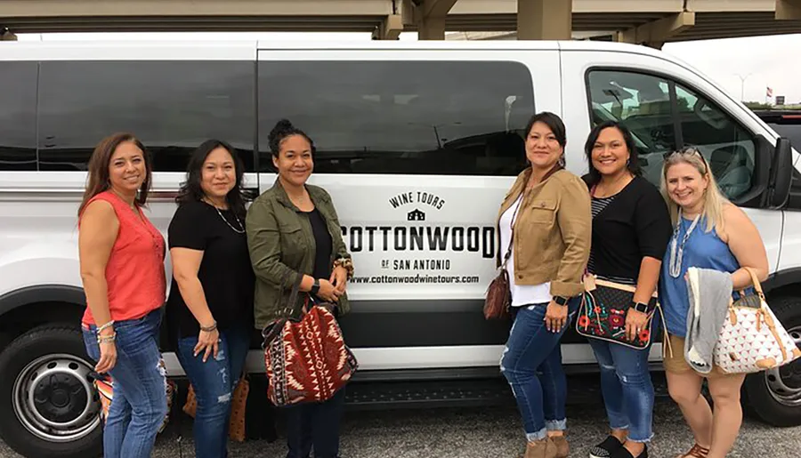 A group of six women pose smiling in front of a COTTONWOOD Wine Tours van.