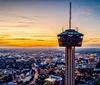 The image captures a breathtaking aerial view of a city at sunset with a prominent tower in the foreground set against a vibrant sky