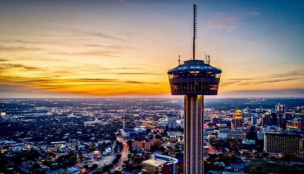 The image captures a breathtaking aerial view of a city at sunset with a prominent tower in the foreground set against a vibrant sky