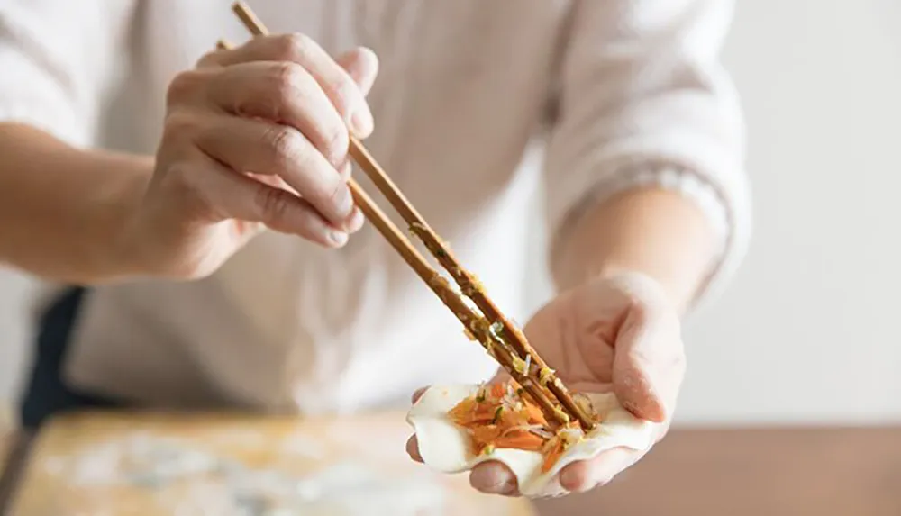 A person is using chopsticks to carefully place fillings into a dumpling wrapper