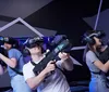 Three people are posing and smiling in a virtual reality gaming arena holding VR guns and wearing VR headsets