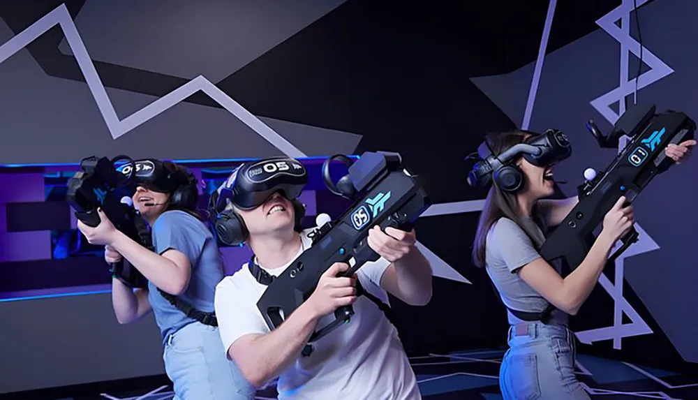 Three people are wearing virtual reality headsets and wielding gun-shaped controllers likely engaged in an immersive VR gaming experience