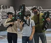 Three people are posing and smiling in a virtual reality gaming arena holding VR guns and wearing VR headsets