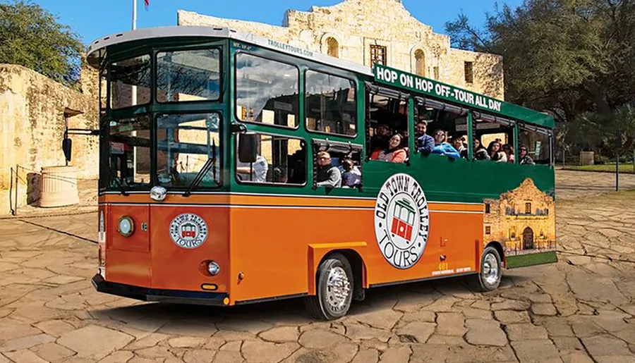 The image shows a colorful sightseeing trolley bus with passengers aboard, indicating a hop-on-hop-off tour service under a clear sky with historical architecture in the background.