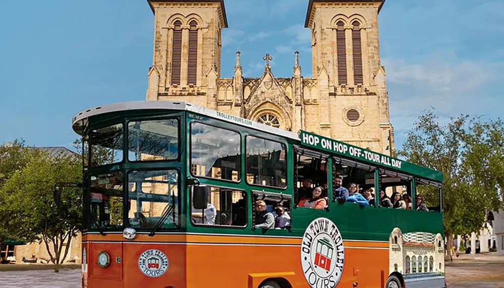 A hop-on hop-off tourist trolley bus is parked in front of a historic cathedral with passengers looking out