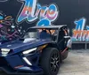 A blue and black three-wheeled vehicle is parked in front of a colorful mural that spells out SAN ANTONIO TEXAS