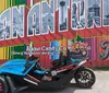 A blue and black three-wheeled vehicle is parked in front of a colorful mural that spells out SAN ANTONIO TEXAS