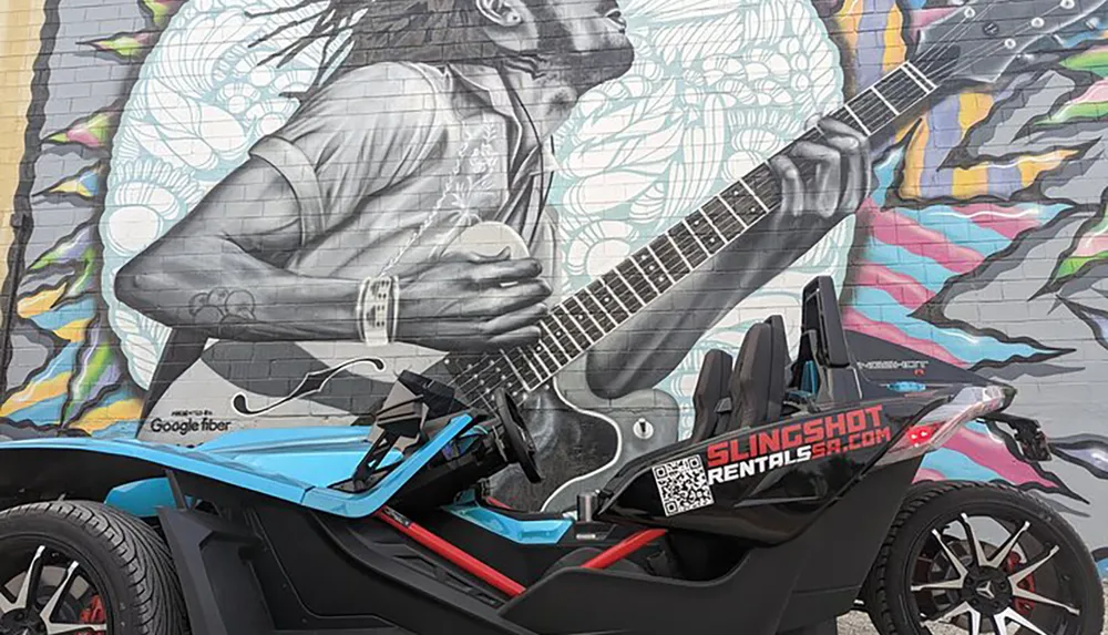 A three-wheeled vehicle is parked in front of a vibrant mural depicting a person playing an electric guitar