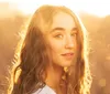 A young woman with wavy hair is backlit by a warm golden sunset creating a soft glowing portrait amidst a blurred natural background