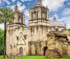 The image showcases the historic stone arches and architecture of an ancient mission against a backdrop of a bright blue sky with fluffy clouds