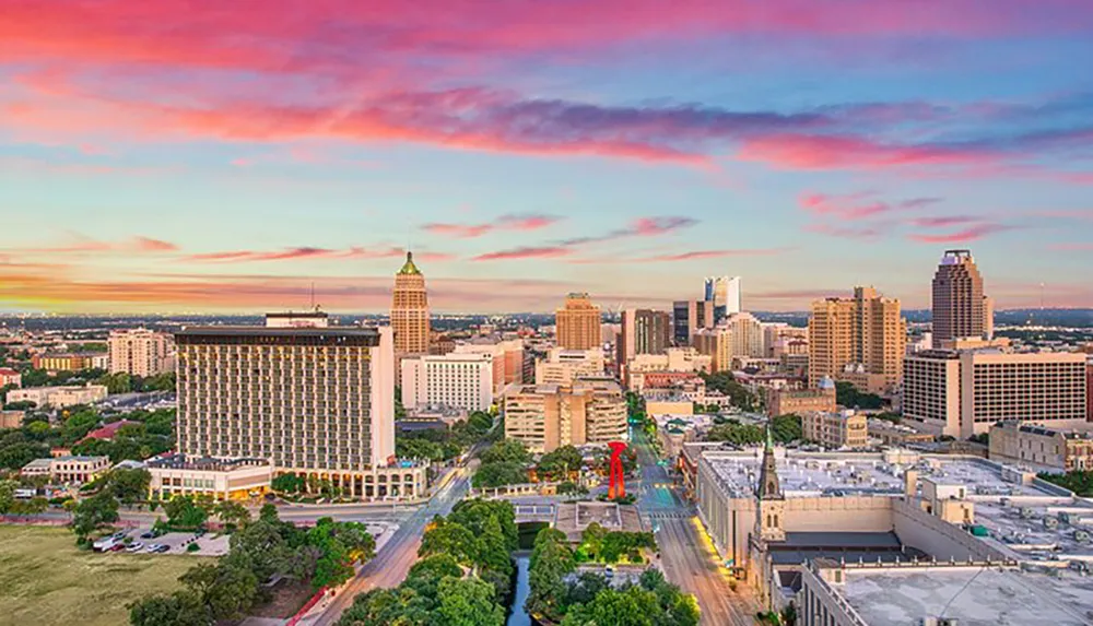 The image displays a panoramic view of a city skyline at dusk characterized by a mix of high-rise buildings against a backdrop of a vibrant sunset with pink and blue hues in the sky