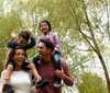 A happy family with two adults and two children are enjoying their time outdoors with the children sitting on the adults shoulders