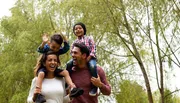 A happy family with two adults and two children are enjoying their time outdoors, with the children sitting on the adults' shoulders.