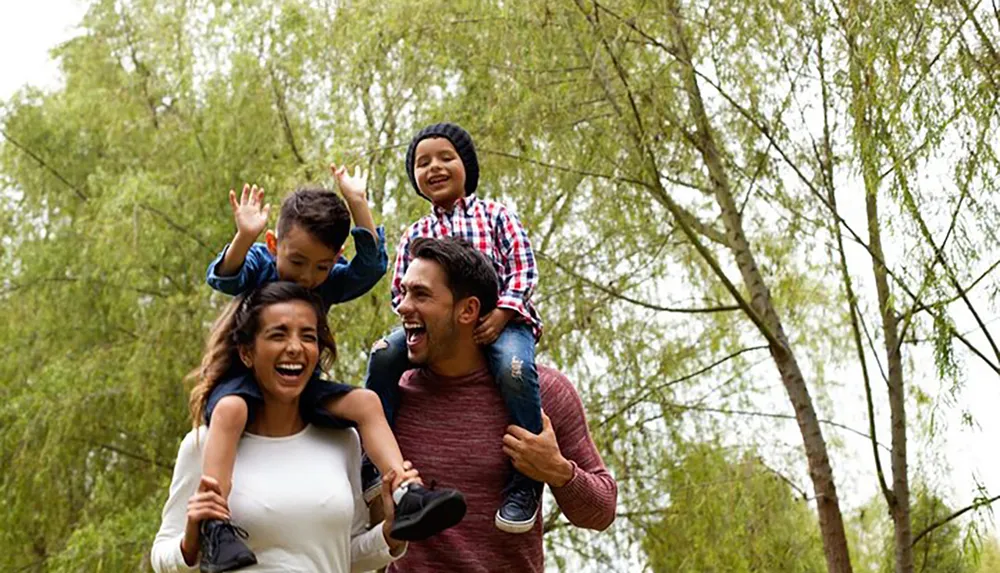 A happy family with two adults and two children are enjoying their time outdoors with the children sitting on the adults shoulders