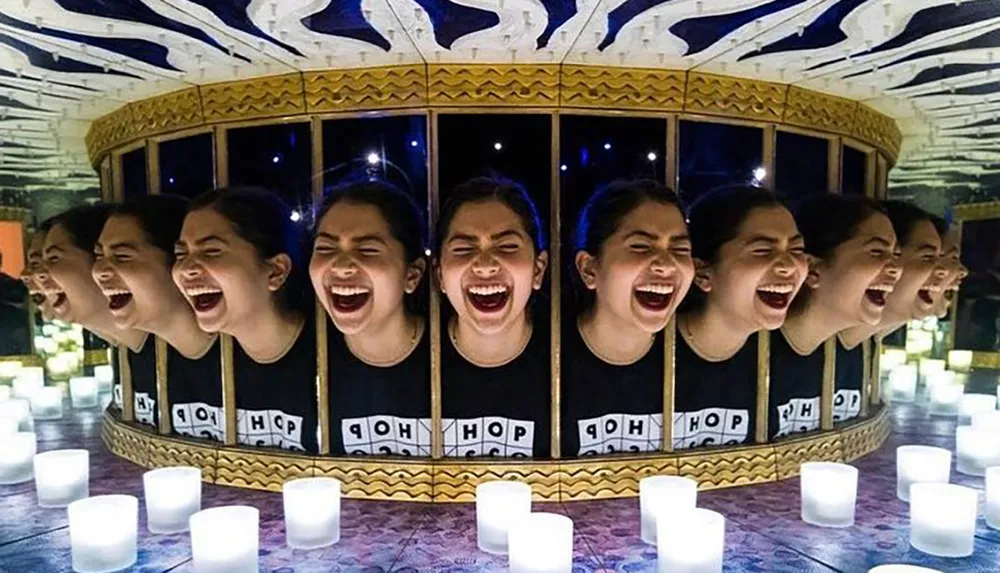 The image shows a person laughing repeated multiple times due to the reflection in surrounding mirrors creating a kaleidoscopic effect