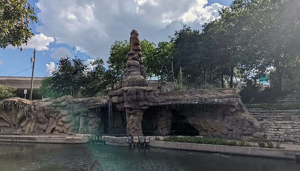 A rock formation with a small waterfall overlooks a tranquil body of water creating a serene landscape