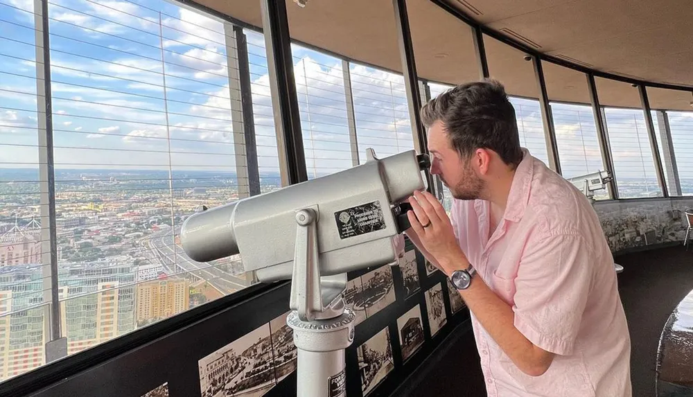 A person is using a coin-operated telescope at a high observation point to view a cityscape