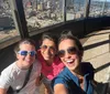 Three people are smiling for a selfie with a cityscape visible from a high vantage point in the background