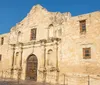 The image shows the historic Alamo mission in San Antonio Texas with its distinctive facade under a bright blue sky