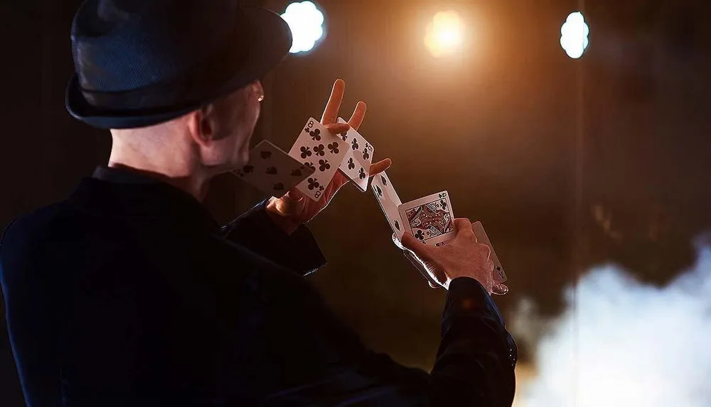 A person in a hat is performing a card trick under stage lights