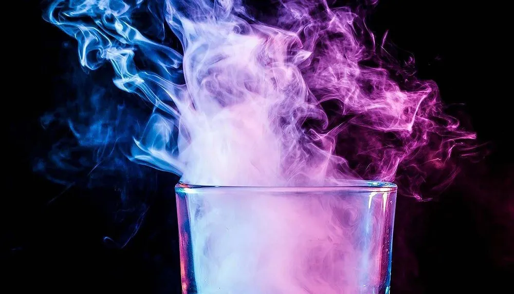 A glass emits swirling clouds of vibrant blue and pink smoke against a dark background