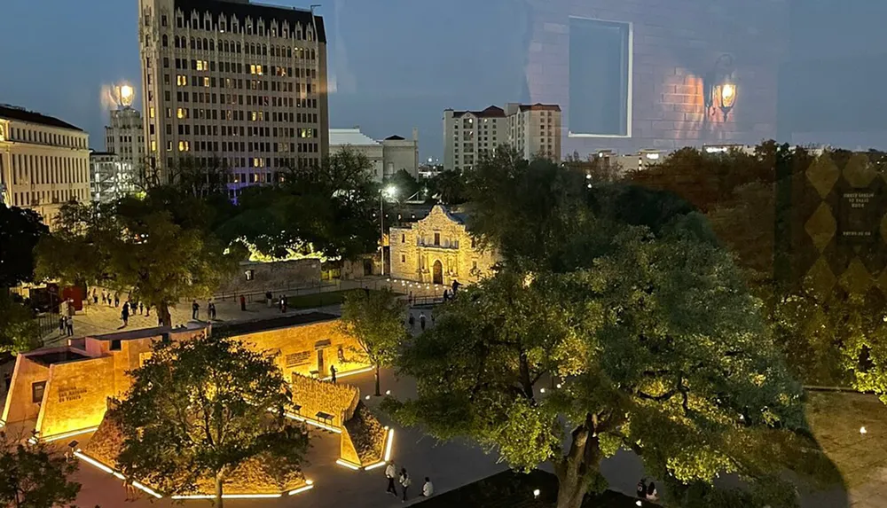 The image shows a nighttime view of a historic building and surrounding area illuminated by lights with the city skyline in the background