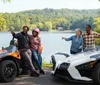 The image shows two Polaris Slingshot three-wheeled vehicles driving down a scenic road with passengers wearing helmets