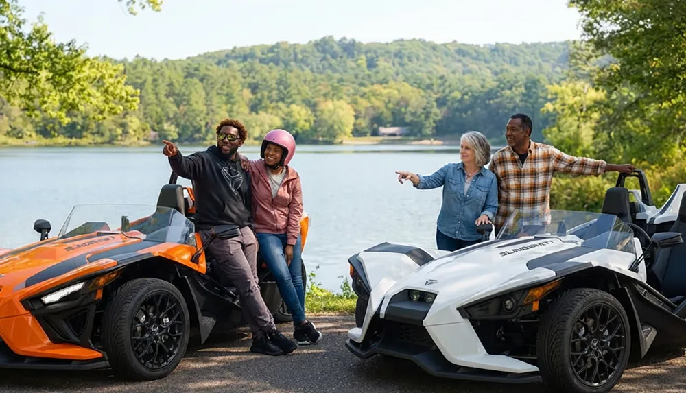 Four people are enjoying a scenic lake view next to orange and white three-wheeled vehicles