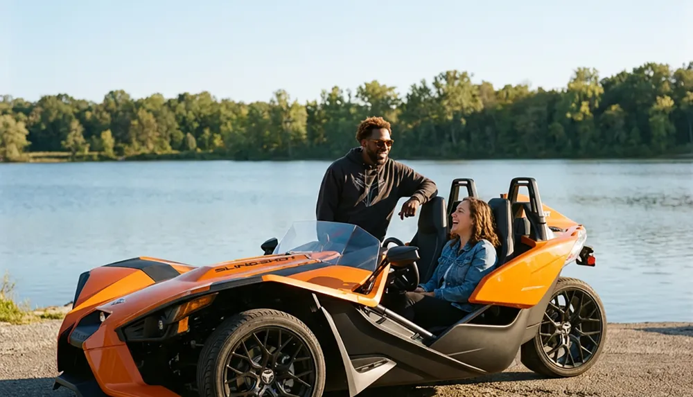 A man and woman share a laugh near a vibrant orange three-wheeled vehicle by a scenic lakeside