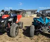 A person in full protective gear is riding a red ATV on a dirt trail kicking up dust and mud