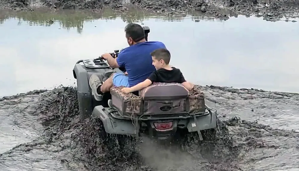 Two people are riding an ATV through a muddy area with water