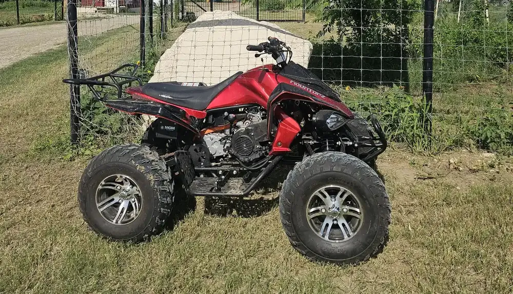 A red all-terrain vehicle ATV is parked on grassy ground near a wire fence