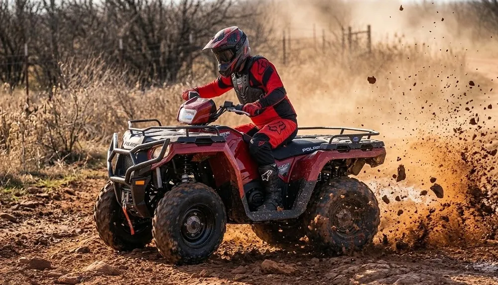 A person in full protective gear is riding a red ATV on a dirt trail kicking up dust and mud
