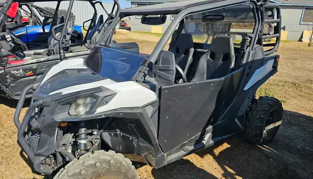 The image shows a side-by-side off-road vehicle parked on a dirt lot with others in the background