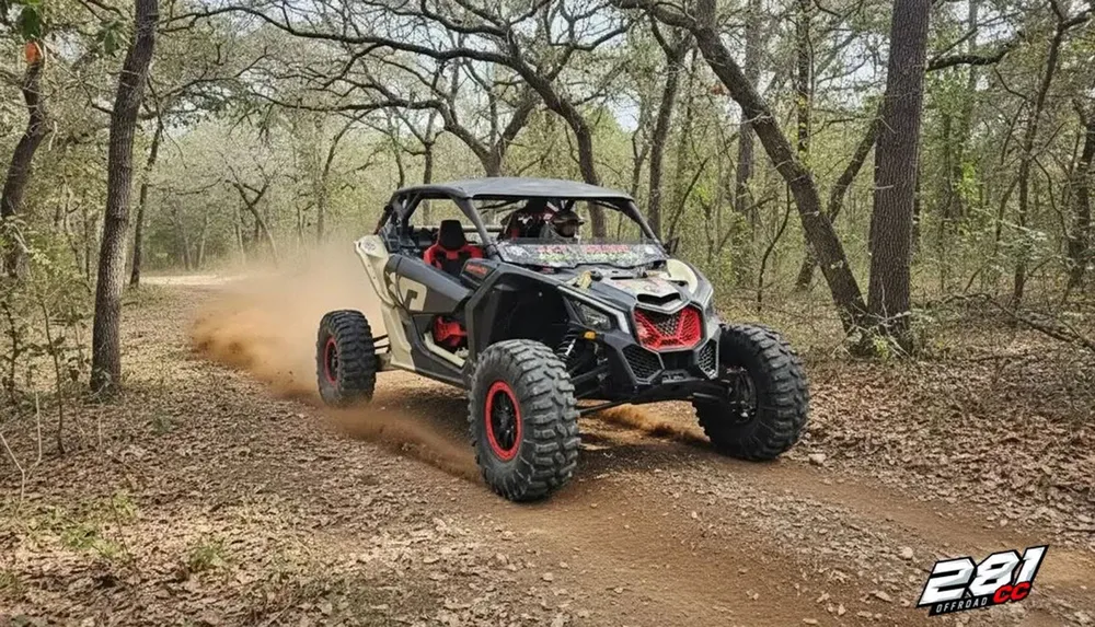 A rugged off-road vehicle is driving through a forest trail kicking up dust as it speeds along