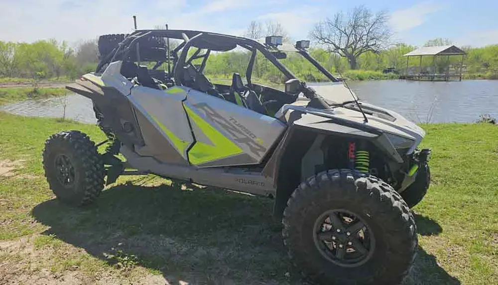 A gray and neon green off-road ATV is parked on grass near a body of water