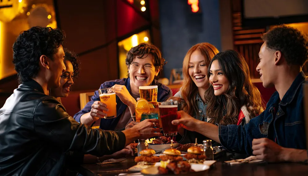 A group of joyful friends is toasting with drinks at a restaurant table filled with food