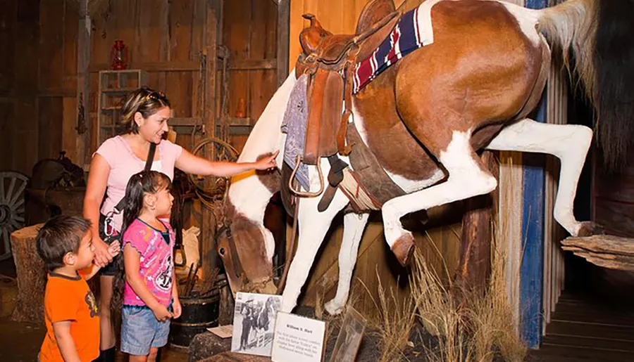 A woman and two children are interacting with a display of a horse in a museum-like setting.