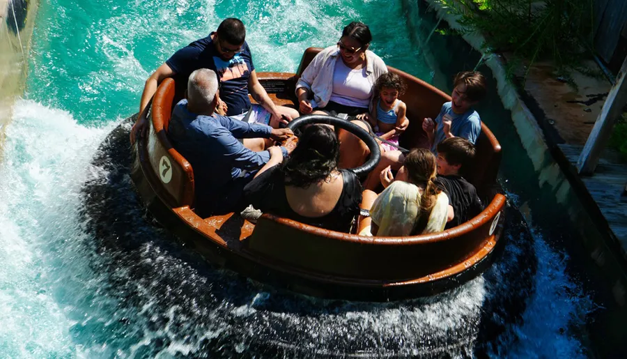 A group of people, expressing a range of emotions from joy to apprehension, are enjoying a ride in a circular raft splashing down a water slide in an amusement park.