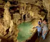 A family is admiring an underground pool in a beautifully lit cave with intricate rock formations surrounding them