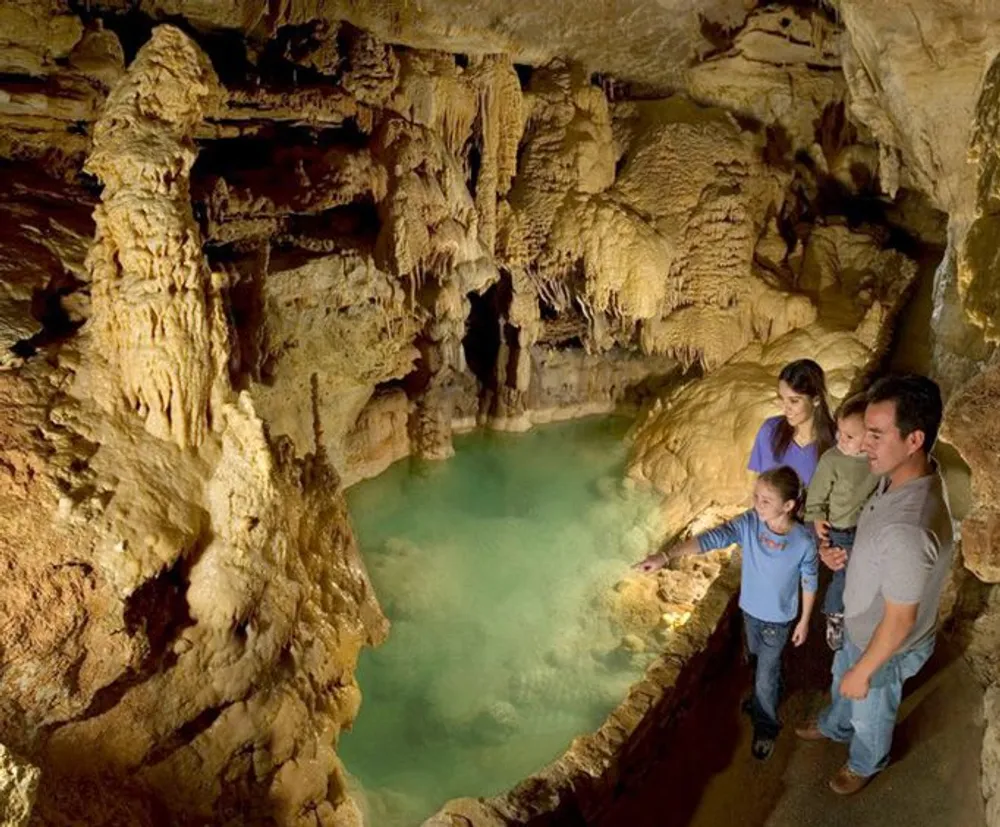 A family is admiring an underground pool in a beautifully lit cave with intricate rock formations surrounding them