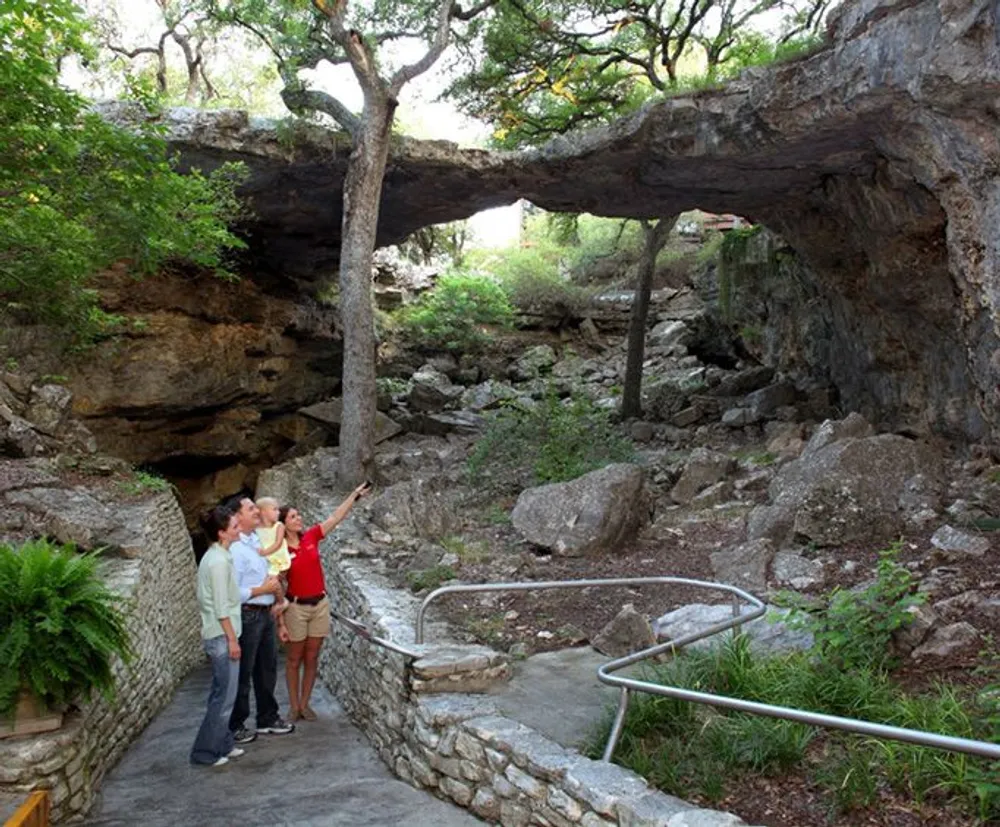 A group of people is observing a natural rock bridge in a wooded area