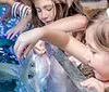 Children are seen delightfully interacting with aquatic animals touching a ray in a touch pool and meeting penguins in an inset image reflecting an educational and engaging experience at an aquarium
