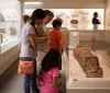 Visitors are closely examining ancient artifacts at a museum exhibit with a focus on a sarcophagus