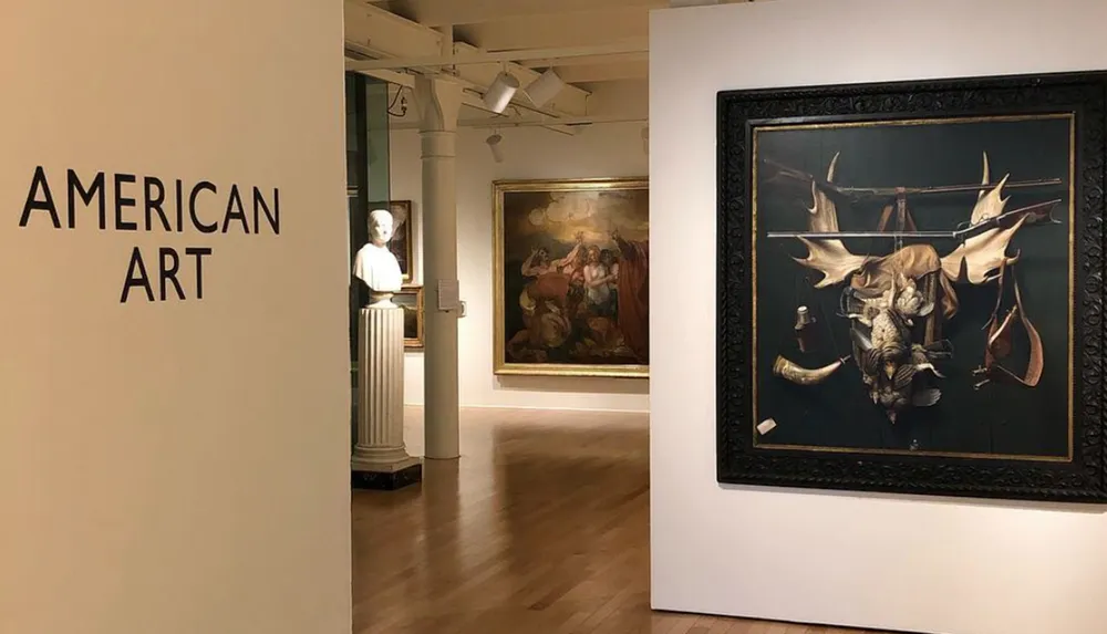 The image shows a gallery view with a wall sign reading AMERICAN ART including a sculpture on a pedestal and paintings one prominently displaying a darkly-lit assemblage of animal skulls and horns