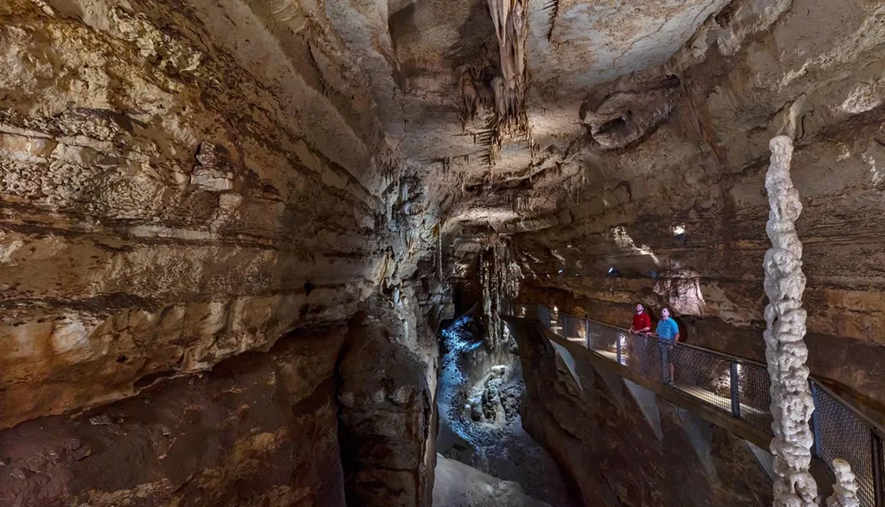 Visitors explore a well-lit underground cave filled with geological formations along a metal walkway