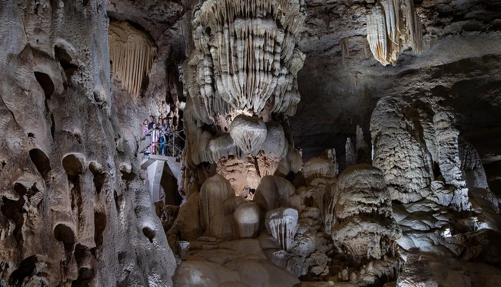 Visitors explore a cavernous space adorned with impressive stalactites and stalagmites within a dimly lit cave