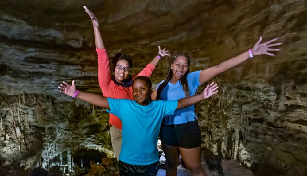 Three joyful individuals are posing with arms raised in a cave-like setting expressing happiness or excitement